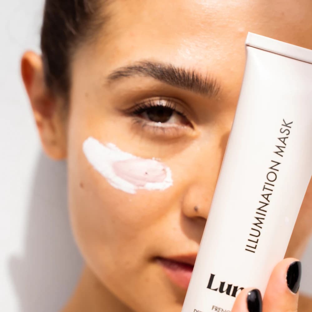 A person applying a cream face mask to their cheek