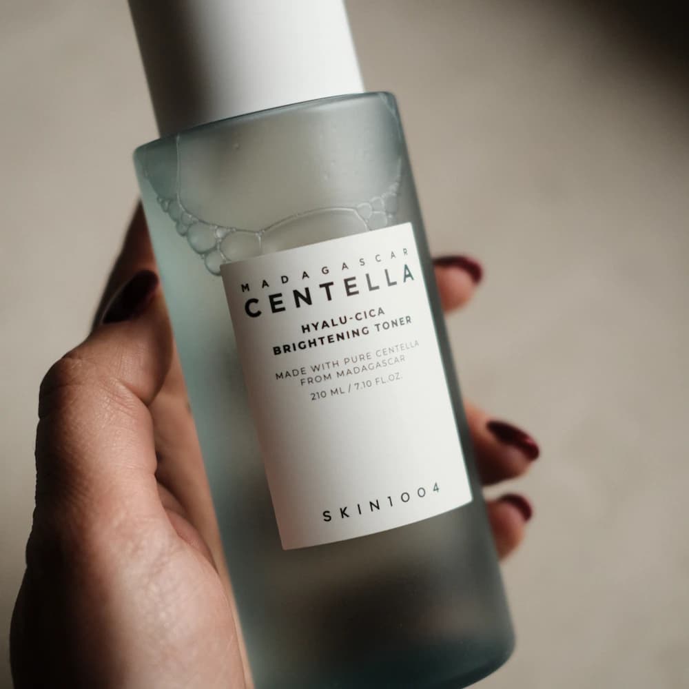 A hand holding a translucent skincare toner bottle